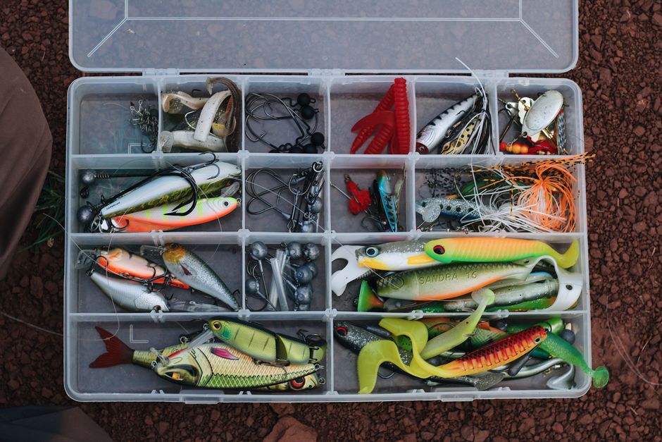 A top view of a tackle box filled with various colorful fishing lures and equipment.