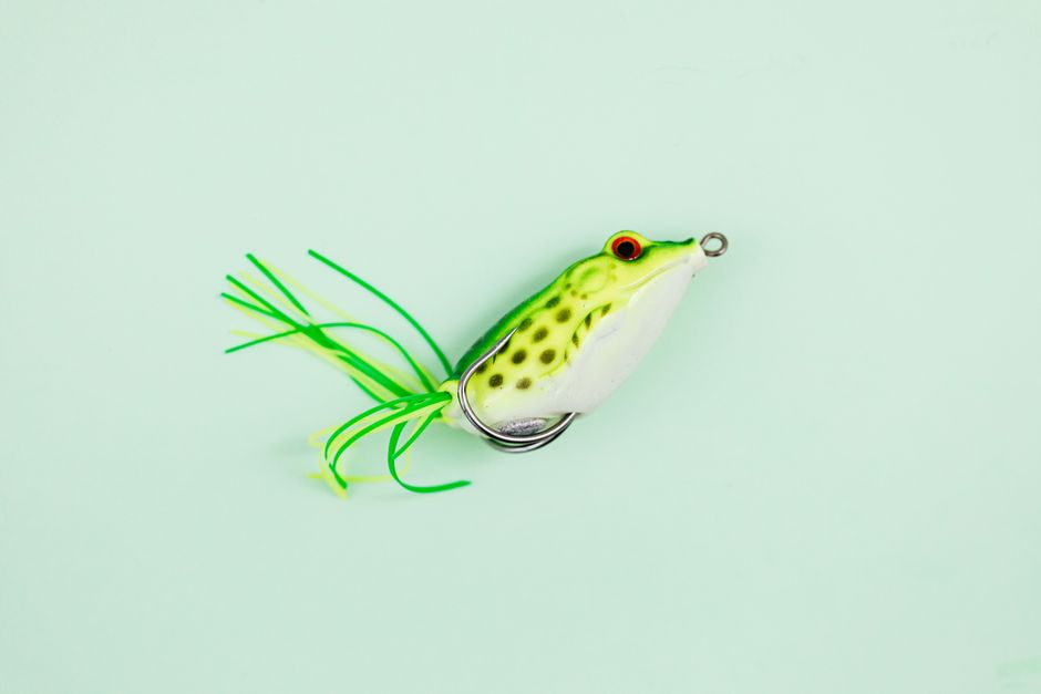 Frog-shaped fishing lure with vibrant green hues on a solid surface.