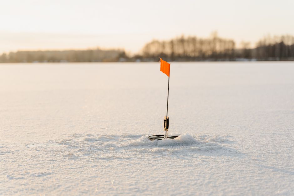 A bright orange flag marks a spot on a snow-covered ice during a clear winter day.